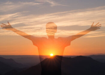 Man with arms raised with sunset in the mountains in the background. Person worshiping or thanking God. Success and happiness concept.